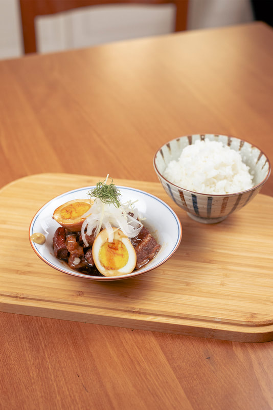 A bowl of Kakuni topped with thinly sliced onions. Next to the Kakuki, a bowl of white rice.