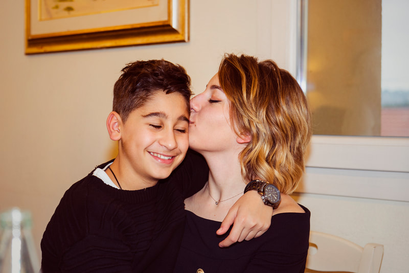 A blond teenage girl kissing his little brother on the cheek.